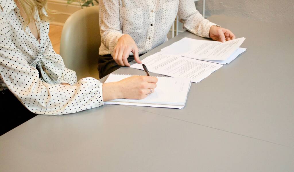 Two women look at mortgage contracts, one of the professionals is making notes.