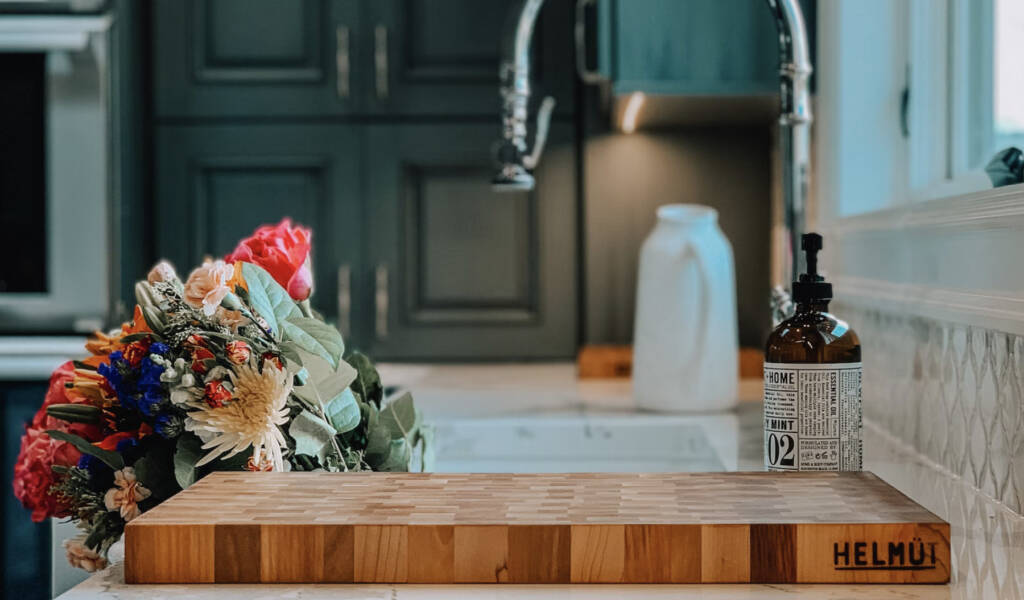 A cutting board on a brand new kitchen table with flowers in the sink.