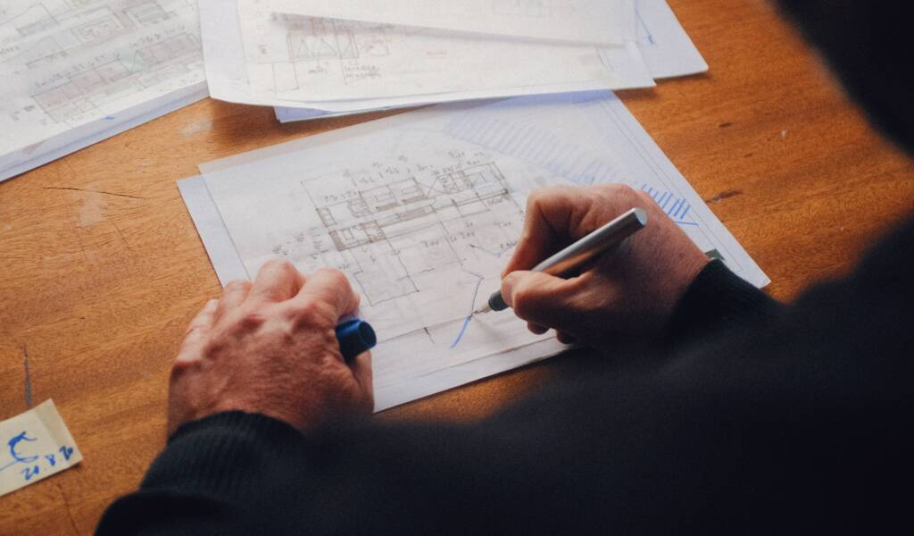 Man writing blue prints on a wooden table.