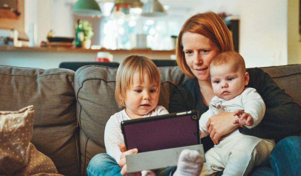 A mother and her children sitting on their living room sofa. They are looking at their tablet computer.